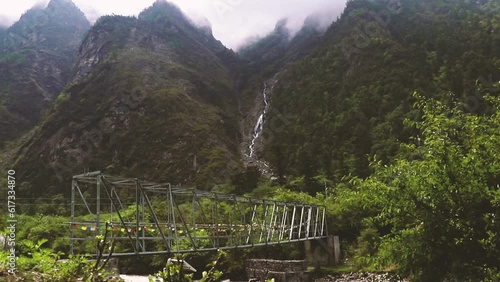 Nepali metal bridge surrounded by mountains with a waterfall - Langtang trek, Nepal photo