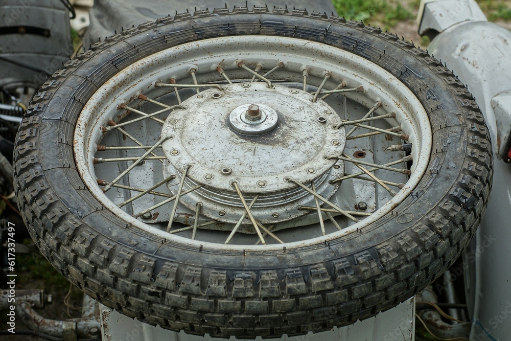 one old retro iron dirty heavy with iron spokes motorcycle spare wheel made in the ussr on top of an iron gray metal sidecar