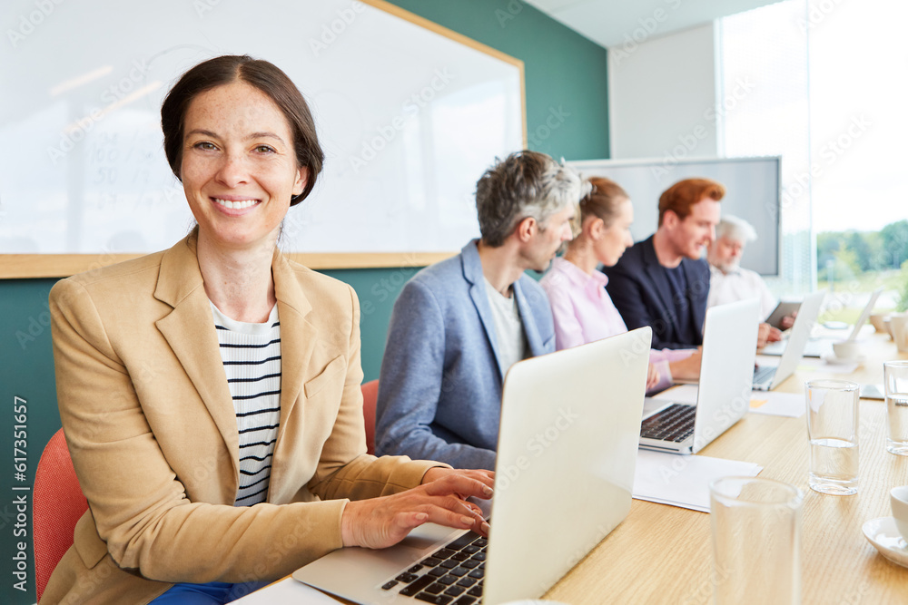 Smiling businesswoman using laptop while sitting by colleagues working at conference table in office
