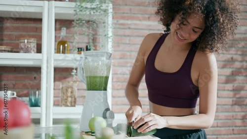 Video of sporty young woman making a vegetable green smoothie in the kitchen at home. photo