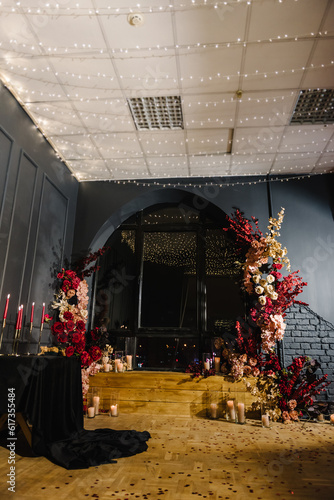 Romantic date in restaurant. Luxury candlelight dinner setup table for couple on Valentine's day. Location with arch, wall, photozone decoration flowers, decor candles for surprise marriage proposal.
