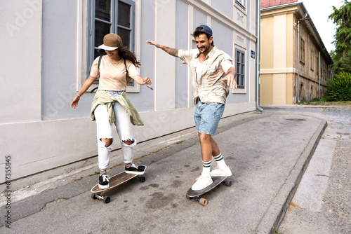 Tourists couple skateboarders riding skates. Happy young travelers longboarding together on sunset on pavement. Stylish man and woman in trendy outfit skating outdoors in touristic destination streets photo