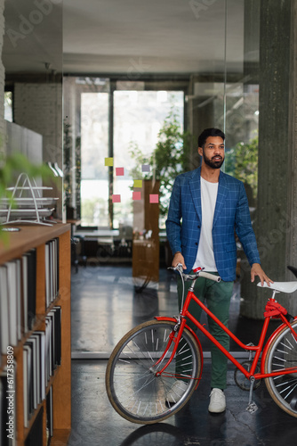 Young multiracial man with bicyckle in office.