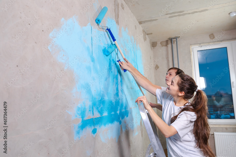 Couple in new home during repair works painting wall together. Happy family holding paint roller