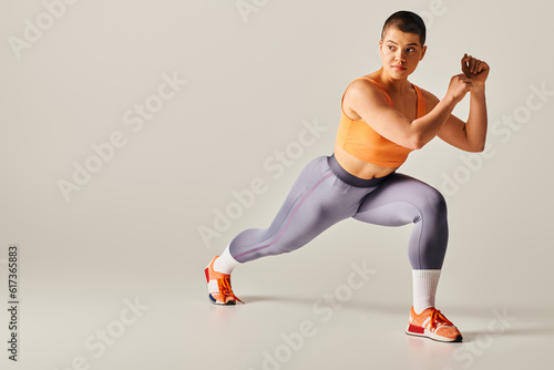 self-esteem, body positivity, young short haired woman doing lunges on grey background, curvy fitness model in sportswear, athletic and confident. empowerment, motivation, working out