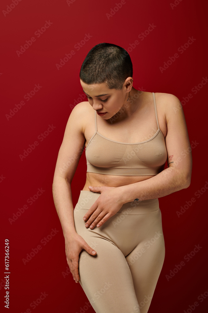 Naklejka premium body positive, self-esteem, young woman with short hair and tattoo posing on burgundy background, dark red, curvy fashion, comfortable in skin, female underwear, fashion model, body type