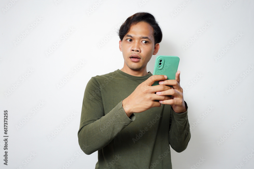 Young Asian man looking his mobile phone with surprised expression Young Asian man looking his mobile phone with surprised expression