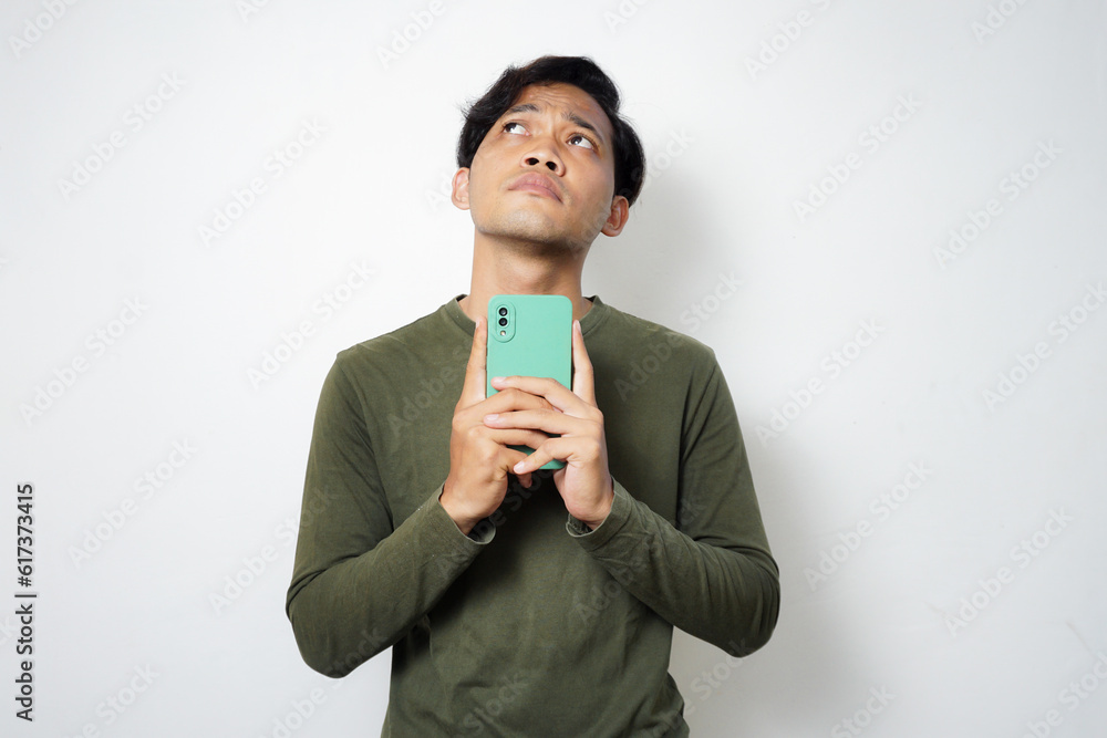 Adult Asian man think something while typing on his mobile phone Adult Asian man think something while typing on his mobile phone