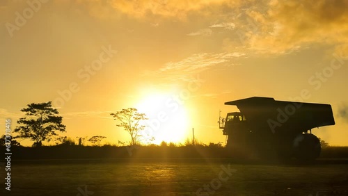 A mining truck passes along a hauling road, against the backdrop of a scenic sunset silhouette, shining under the warm rays of sunshine