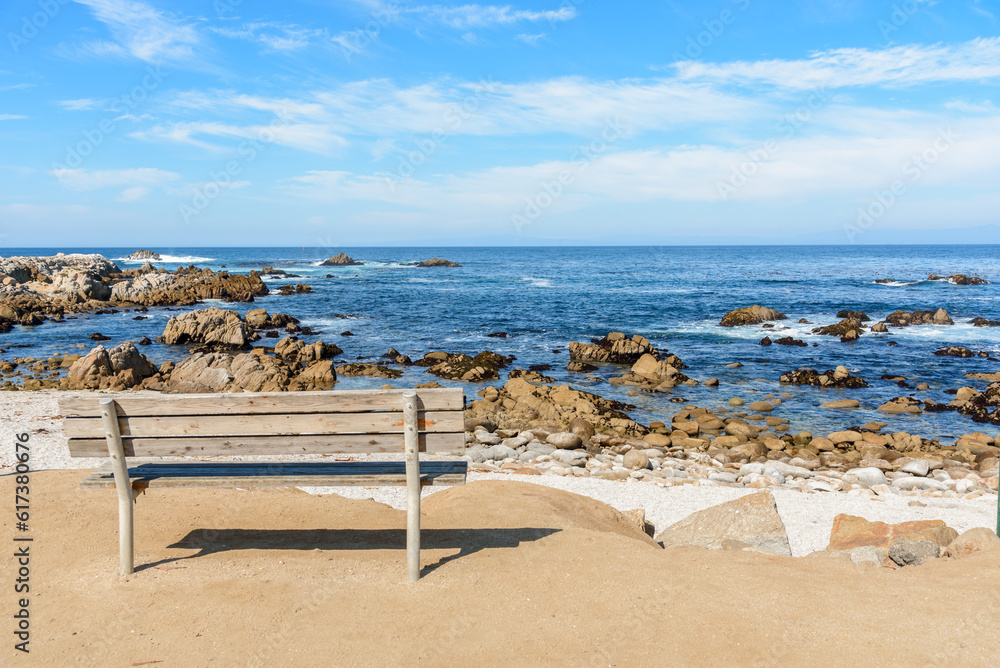Empty wooden bench facing a rocky beach and the ocean on a sunny fall day