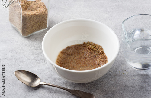 A bowl with ground flax and water, a jar of ground flax and a jug of water on a gray textured background. Cooking a vegan flax egg