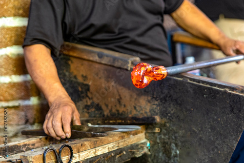 Craftsman cutting and blowing the glass in fusing temperature to make a bottle with the old technique of glass blowing, this is a very old and craft technique. Concept craftsmen.