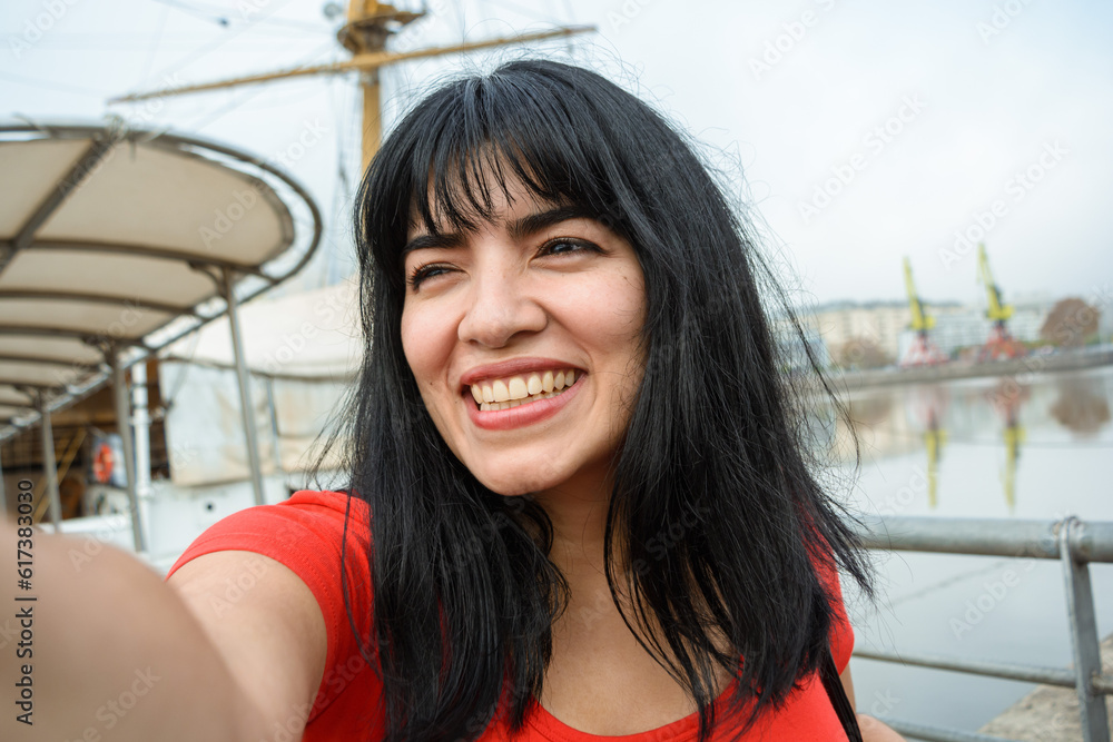 selfie portrait of young latin woman of venezuelan ethnicity dressed in red, smiling happy outdoors