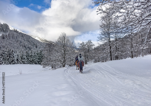Two horse riders on snowy pass in French Alps.