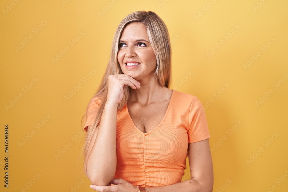 Young woman standing over yellow background thinking worried about a question, concerned and nervous with hand on chin Young woman standing over yellow background thinking worried about a question, concerned and nervous with hand on chin