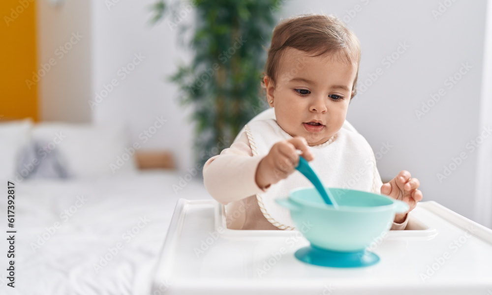 Adorable hispanic baby holding spoon sitting on highchair at bedroom Adorable hispanic baby holding spoon sitting on highchair at bedroom