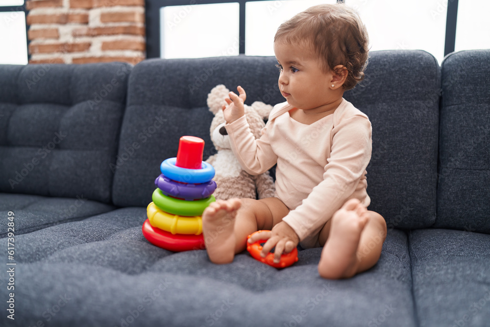Adorable hispanic baby playing with hoops game sitting on sofa at home Adorable hispanic baby playing with hoops game sitting on sofa at home