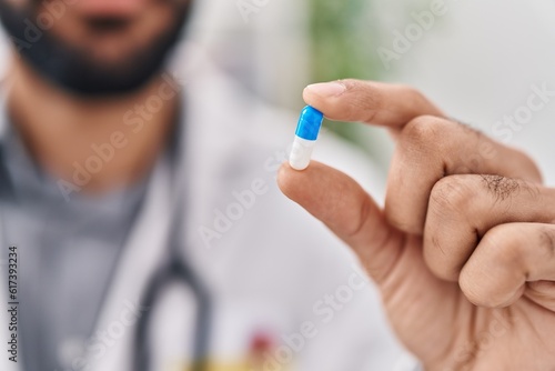 Young hispanic man doctor holding pill at clinic