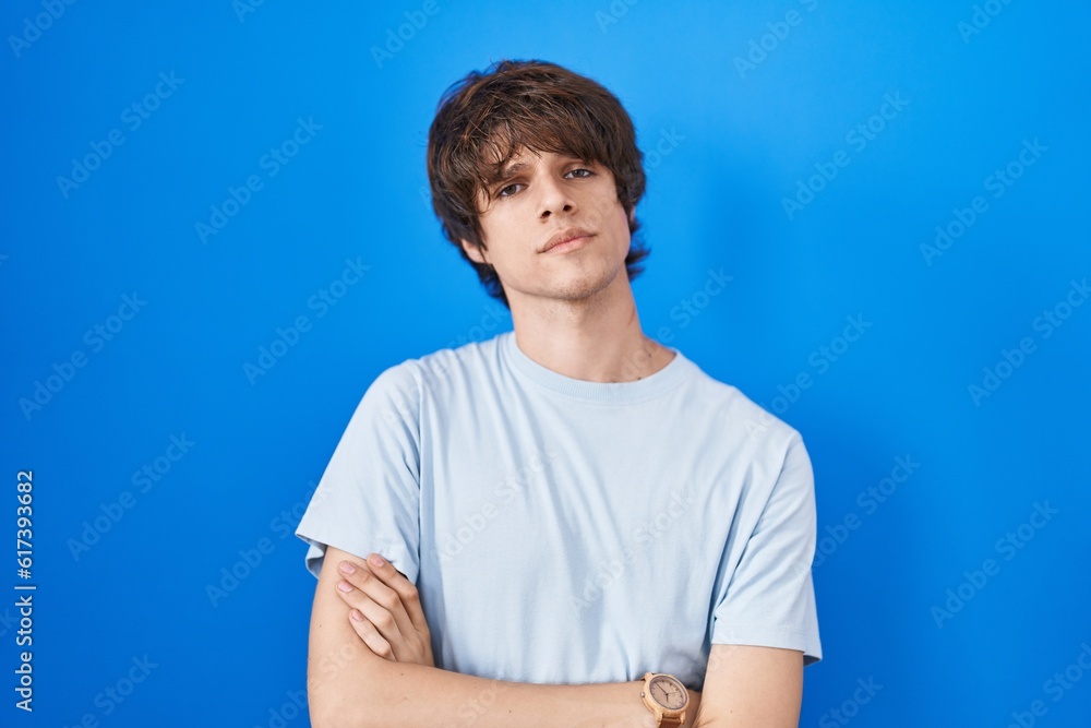 Hispanic young man standing over blue background skeptic and nervous, disapproving expression on face with crossed arms. negative person. Hispanic young man standing over blue background skeptic and nervous, disapproving expression on face with crossed arms. negative person.