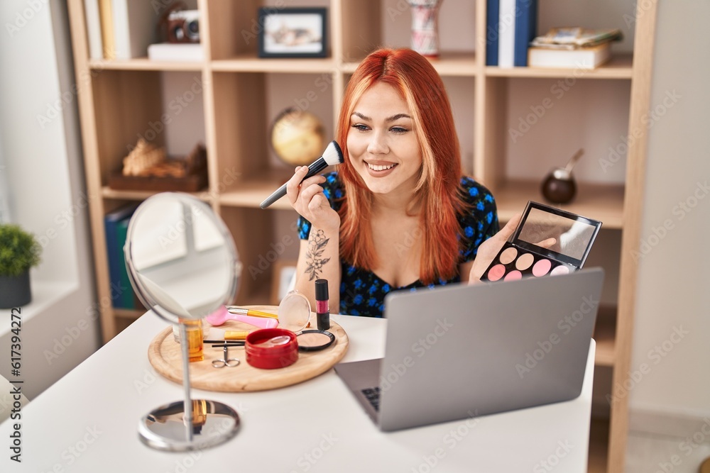 Young caucasian woman applying makeup sitting on table at home