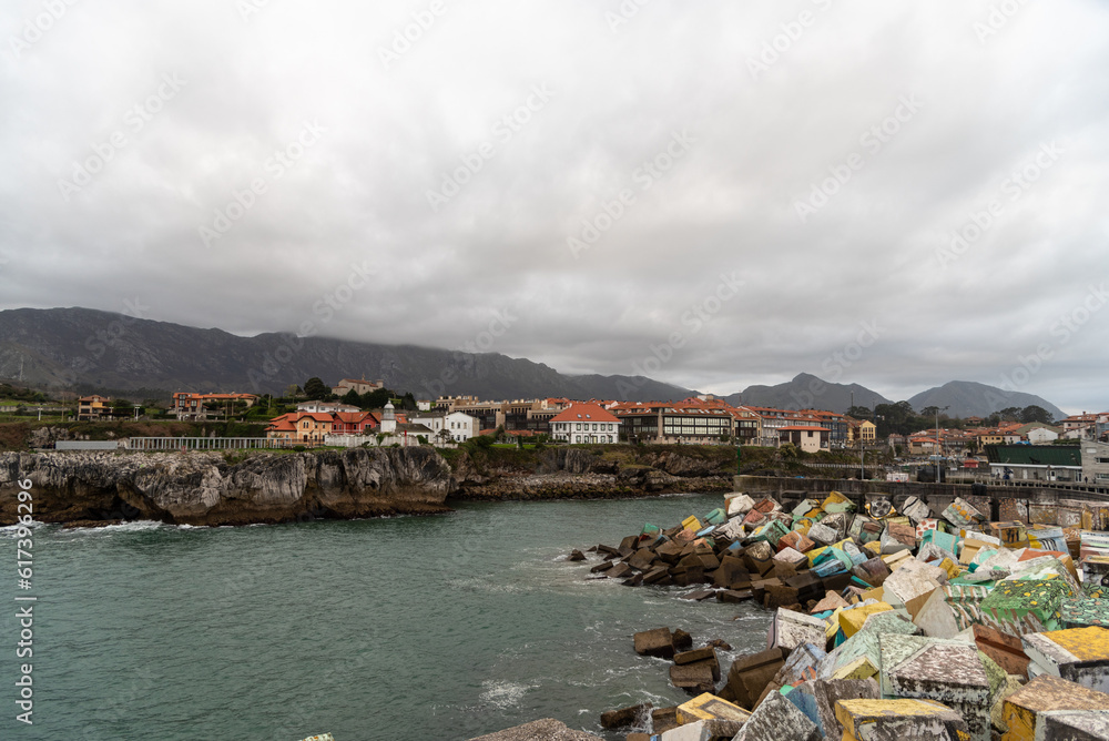 Panoramic view of the coast of Asturias, from the port of the tourist town of Llanes with large painted rocks and calm sea, the cliffs surrounding the town on a cloudy day.