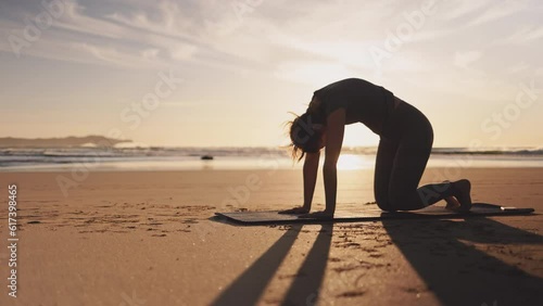 Woman doing workout with dog on ocean beach at sunset. Female doing Yoga and stretching on mat on sand sea shore at sunrise. Strong powerful woman exercises in the morning or evening outdoors. 