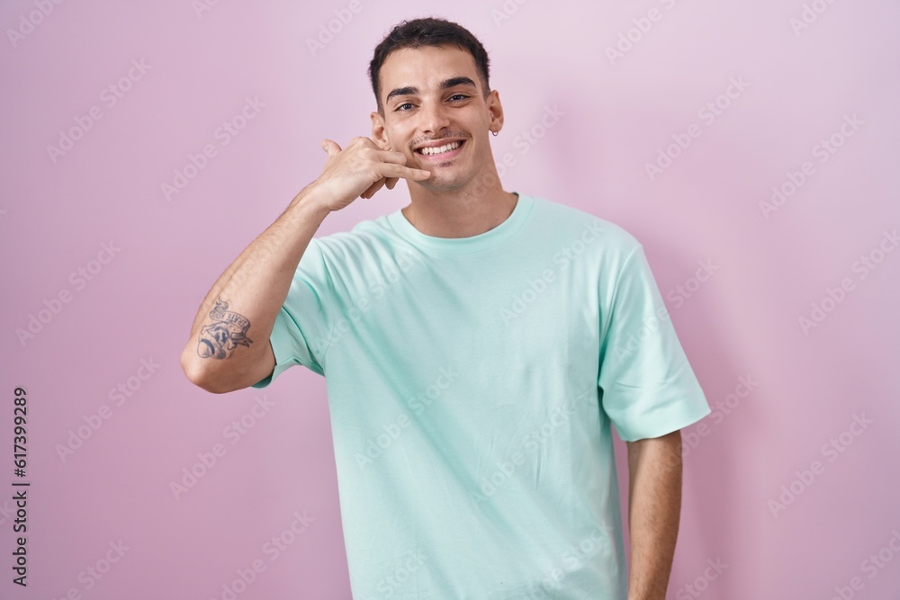 Fototapeta premium Handsome hispanic man standing over pink background smiling doing phone gesture with hand and fingers like talking on the telephone. communicating concepts.