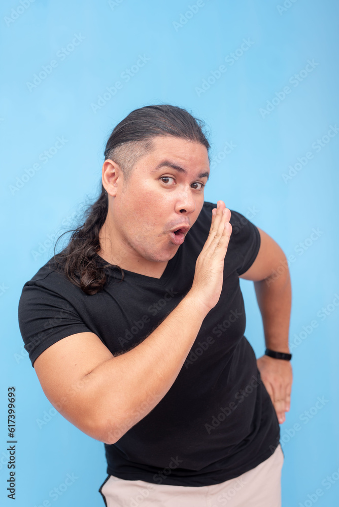 A playful and easygoing biracial male leaning forward and gesturing for a whisper. Isolated on a blue background. A playful and easygoing biracial male leaning forward and gesturing for a whisper. Isolated on a blue background.