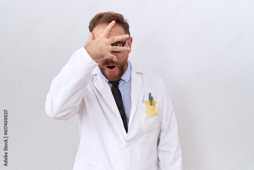 Middle age doctor man with beard wearing white coat peeking in shock covering face and eyes with hand, looking through fingers with embarrassed expression. Middle age doctor man with beard wearing white coat peeking in shock covering face and eyes with hand, looking through fingers with embarrassed expression.