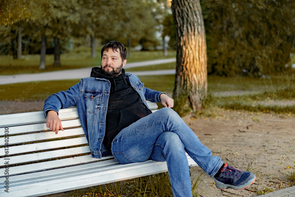 attractive caucasian bearded young man sitting on bench in park on autumn day looking aside attractive caucasian bearded young man sitting on bench in park on autumn day looking aside