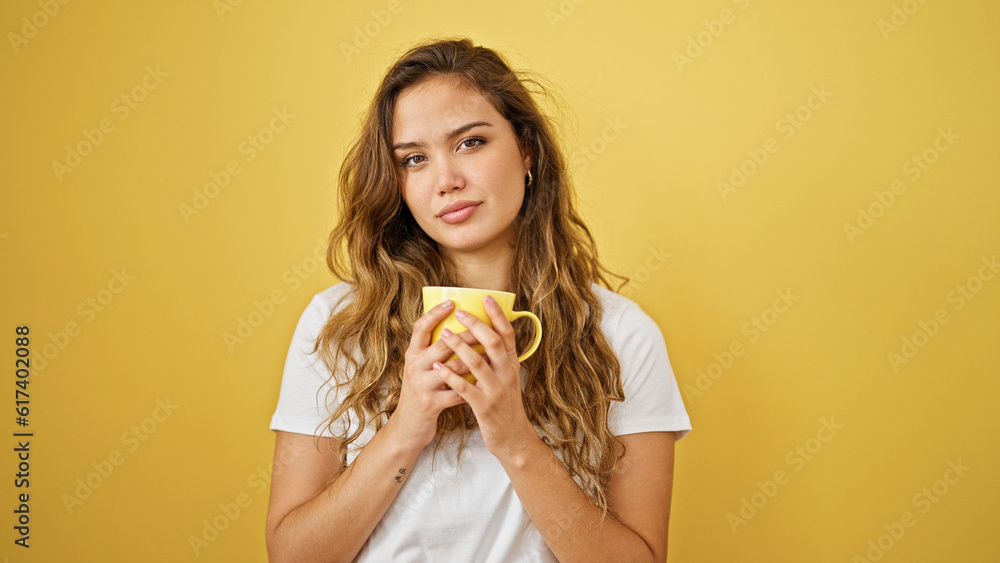 Young beautiful hispanic woman holding cup of coffee with relaxed expression over isolated yellow background