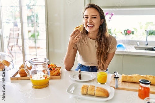 Young beautiful hispanic woman eating bread with jam having breakfast at the kitchen photo