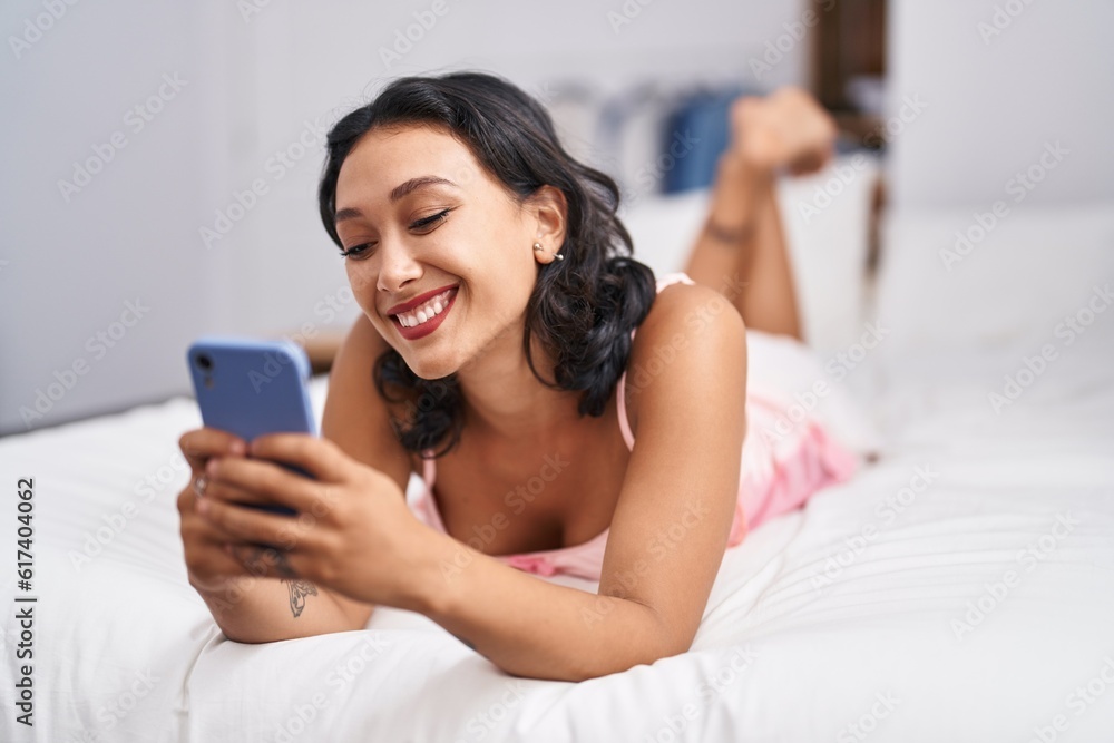 Young beautiful hispanic woman using smartphone lying on bed at bedroom Young beautiful hispanic woman using smartphone lying on bed at bedroom