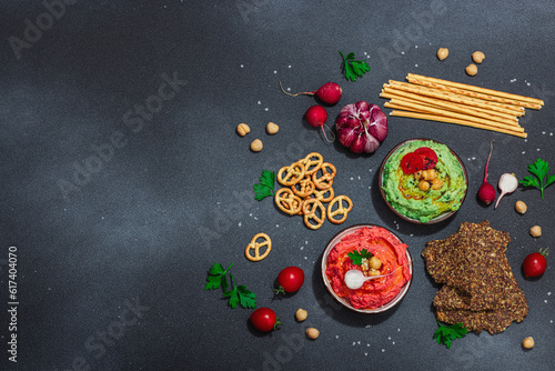 Various hummus dips, fresh vegetables and herbs. Crispy bread snacks, modern vegan healthy food
