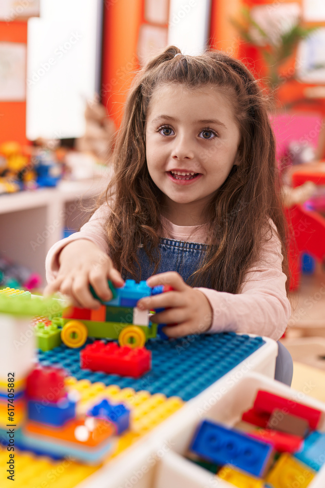 Adorable hispanic girl playing with construction blocks sitting on table at kindergarten Adorable hispanic girl playing with construction blocks sitting on table at kindergarten