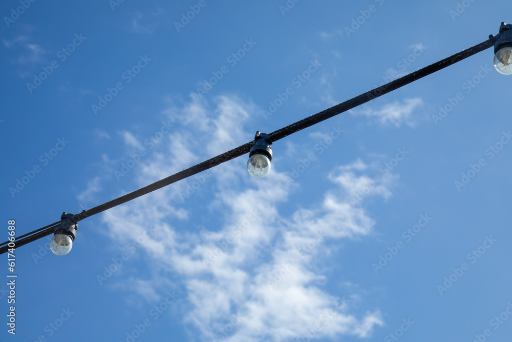 String of outdoor street lights in the bright blue sky in summer String of outdoor street lights in the bright blue sky in summer
