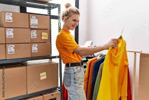 Young blonde woman ecommerce business worker organizing clothes on coat rack at office photo