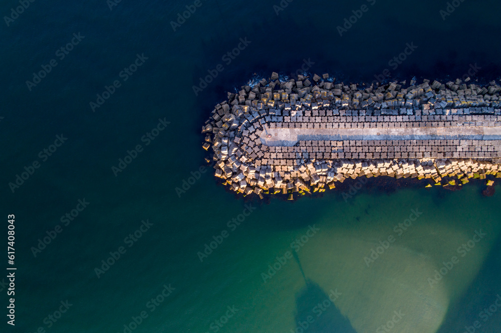 Obraz premium zenithal aerial view of a wave pier in a calm sea.