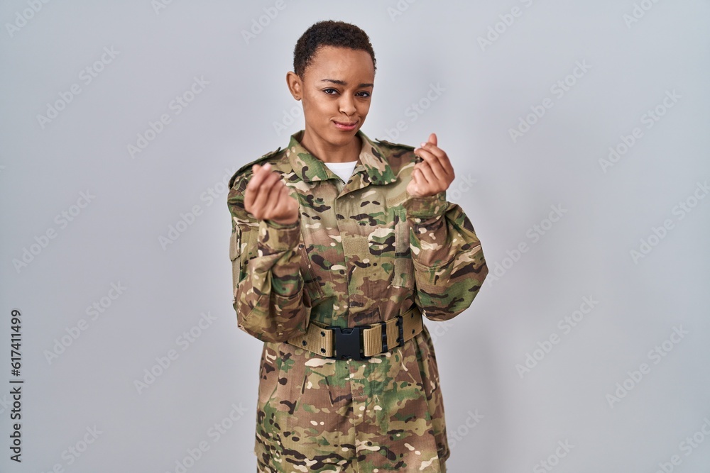 Beautiful african american woman wearing camouflage army uniform doing money gesture with hands, asking for salary payment, millionaire business