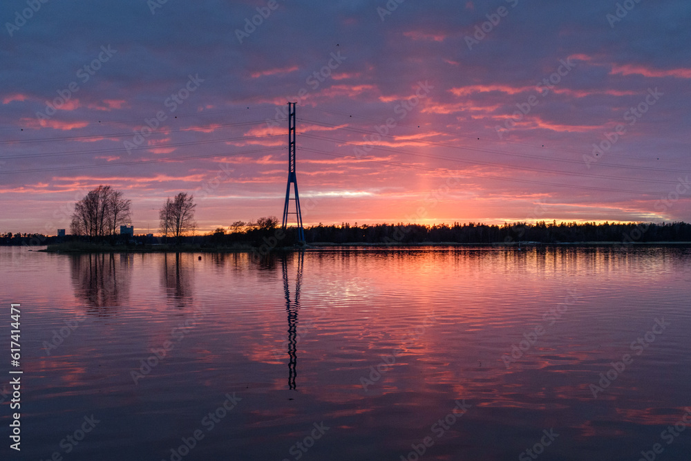 A view of a tall mast and buildings on the coastline of islands near Helsinki, at sunset. A view of a tall mast and buildings on the coastline of islands near Helsinki, at sunset.