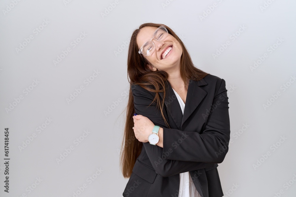 Beautiful brunette woman wearing business jacket and glasses hugging oneself happy and positive, smiling confident. self love and self care Beautiful brunette woman wearing business jacket and glasses hugging oneself happy and positive, smiling confident. self love and self care
