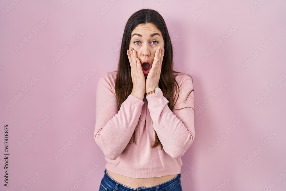Young brunette woman standing over pink background afraid and shocked, surprise and amazed expression with hands on face Young brunette woman standing over pink background afraid and shocked, surprise and amazed expression with hands on face