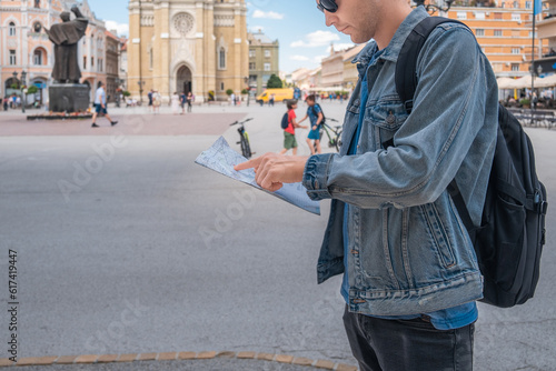 Man tourist on the square in the town with paper map looking is exploring new city. Handsome male traveler backpacker in sunglasses 