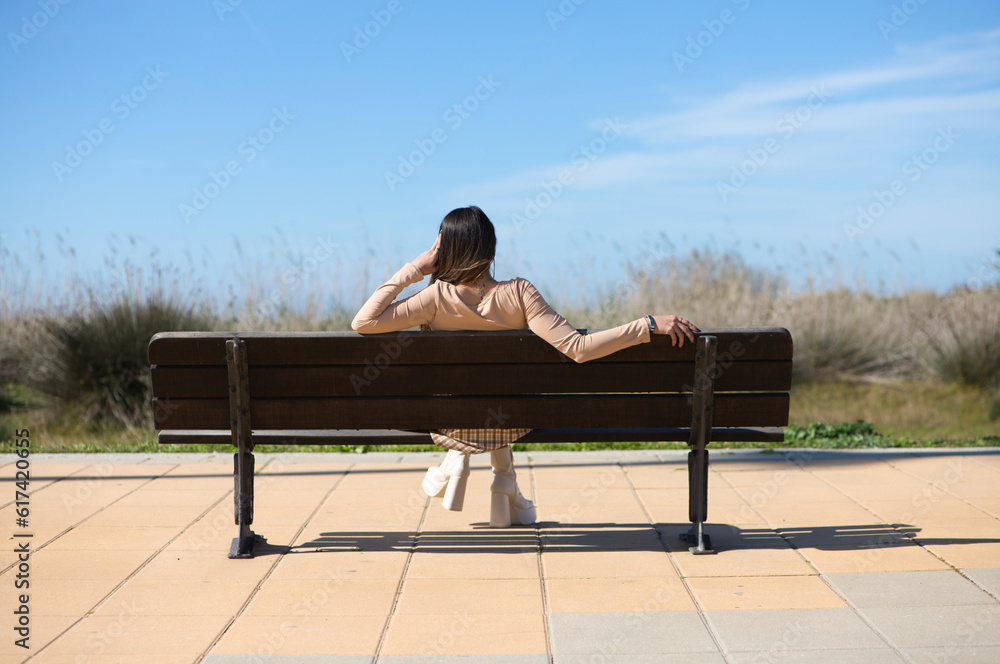 Rear view of a relaxed woman sitting on a bench looking at the horizon of the Atlantic Ocean in Cadiz. The woman is on holiday in the city.