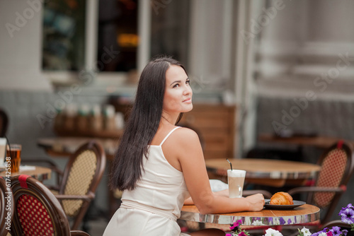 Young beautiful woman is sitting in a french cafe and drinking cappuccino, eating a croissant. Bakery products.