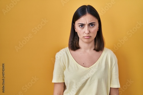 Hispanic girl wearing casual t shirt over yellow background skeptic and nervous, frowning upset because of problem. negative person.