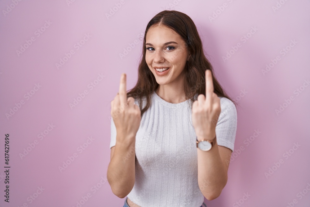 Young hispanic girl standing over pink background showing middle finger doing fuck you bad expression, provocation and rude attitude. screaming excited Young hispanic girl standing over pink background showing middle finger doing fuck you bad expression, provocation and rude attitude. screaming excited