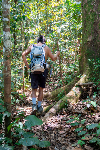 South American male tour guide hiking in the Amazon jungle or rainforest with backpack, a stick, shorts and topless. Adventure in a primary forest in Ecuador. Holidays and traveling. Flora and habitat