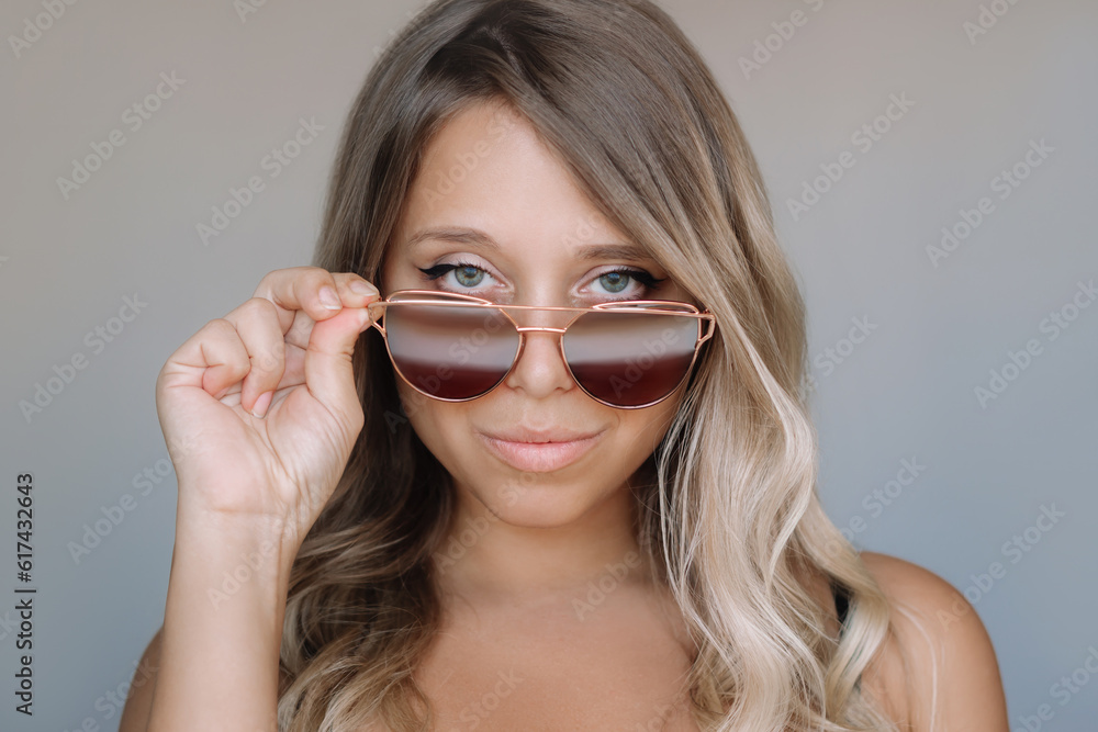 Portrait of a young attractive caucasian blonde woman with wavy hair in stylish sunglasses on a gray background. Beauty and fashion concept Portrait of a young attractive caucasian blonde woman with wavy hair in stylish sunglasses on a gray background. Beauty and fashion concept
