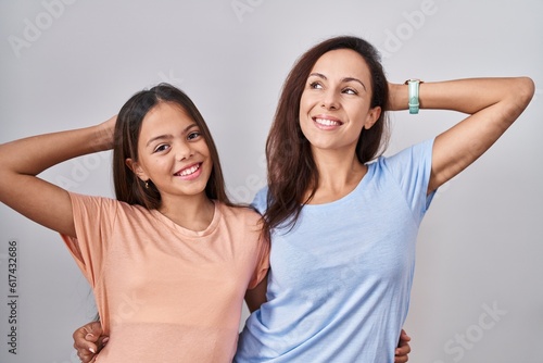Young mother and daughter standing over white background smiling confident touching hair with hand up gesture  posing attractive and fashionable